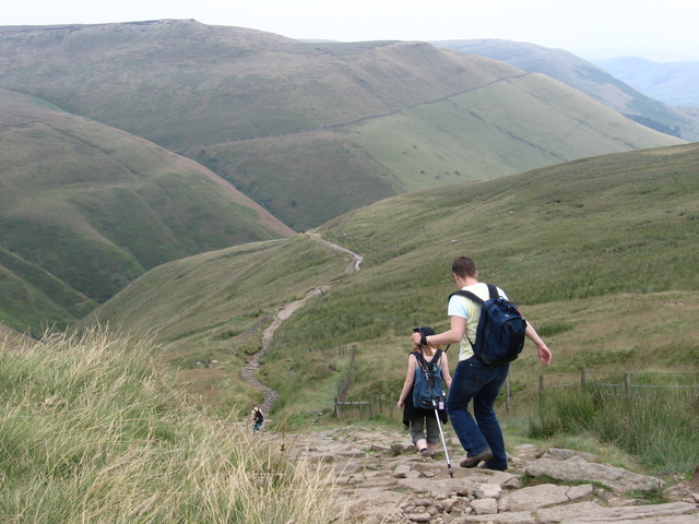 Two ramblers walk down some stone steps on the Pennine way. All around them is green rolling hills