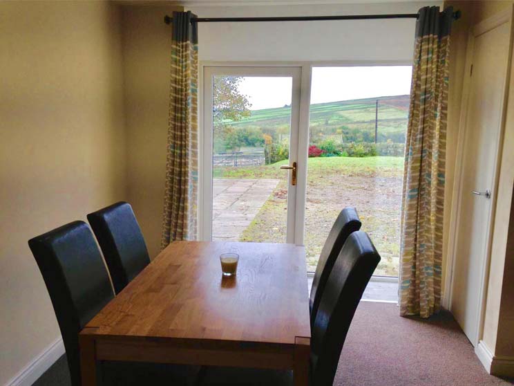 A dining area with four brown leather chairs around a wooden table look out on to countryside views